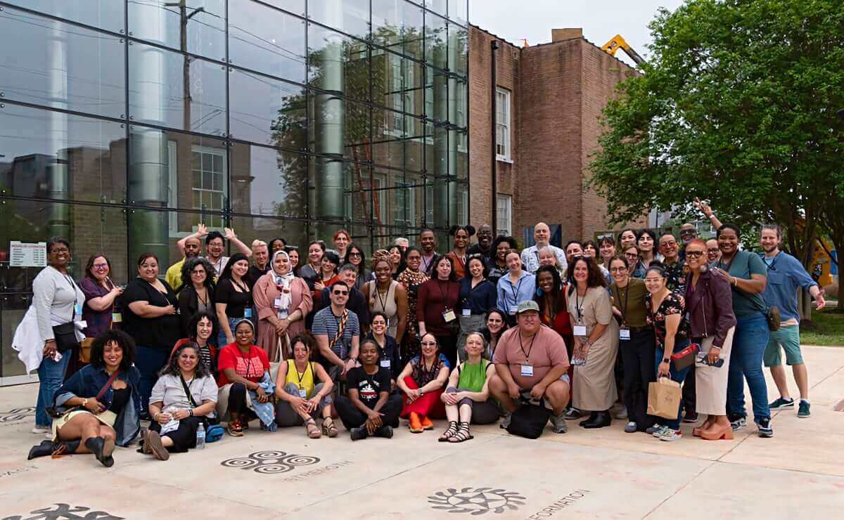 A large group of attendees of the 2025 NPN Partner Meeting stand outdoors and pose for the camera, with people in front sitting down and people on the sides leaning in. Everyone is smiling.
