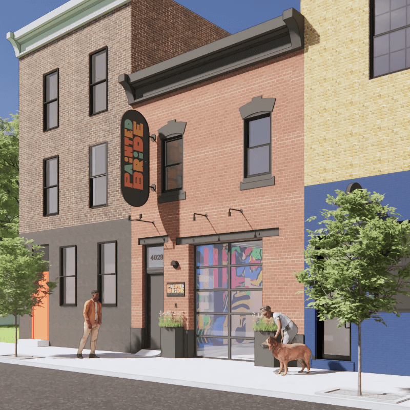 A color rendering of the facade of Painted Bride’s new home. The facade is two stories tall and clad in red brick and connected on either side by other, slightly taller commercial buildings. It has a large, wide window that appears to be a converted garage opening, and a tall, narrow sign approximately six feet tall hanging above the entryway, upon which are printed vertically the words “Painted Bride.”