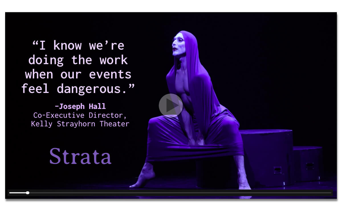 Frame of a performance video by a modern dancer in a stretchy, flexible dance costume that also forms a hood. The dancer has a muscular bare chest and is barefoot, and their face is painted white with dramatically exaggerated blush, eye shadow, lip liner, and lipstick. The dancer is sitting on a corner of a low platform with one leg on either side of the nearest corner of the platform. The space around the dancer is black and empty. A play button floats over the center of the image, and a simplified playback bar stretches across bottom. The aspect ratio of the image along with the play button and the playback bar. On the left side, in light pink type, is the quote, ”I know we’re doing the work when our events feel dangerous. Underneath that in smaller purple letters is the text, "Joseph Hall, Co-Executive Director, Kelly Strayhorn Theater.