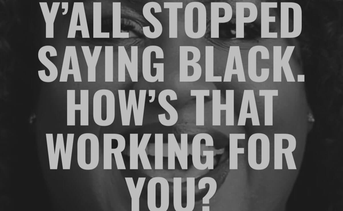 A tightly cropped black and white photo of a smiling Black woman looking into the camera as if about to speak. The text “Y’all stopped saying Black. How’s that working for you?” in large, light gray,  all caps text is stacked in five lines over the woman's face, significantly obscuring her features. The text extends from the top edge of the image to the bottom edge.