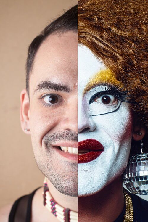 A head shot divided down the middle. The left side shows one half of the face of Anthony Hudson with beard stubble. The right side shows one half of the face of Carla Rossi in a red wig, with severe white makeup, yellow eye shadow and deep red lipstick. Both halves are smiling at the camera.