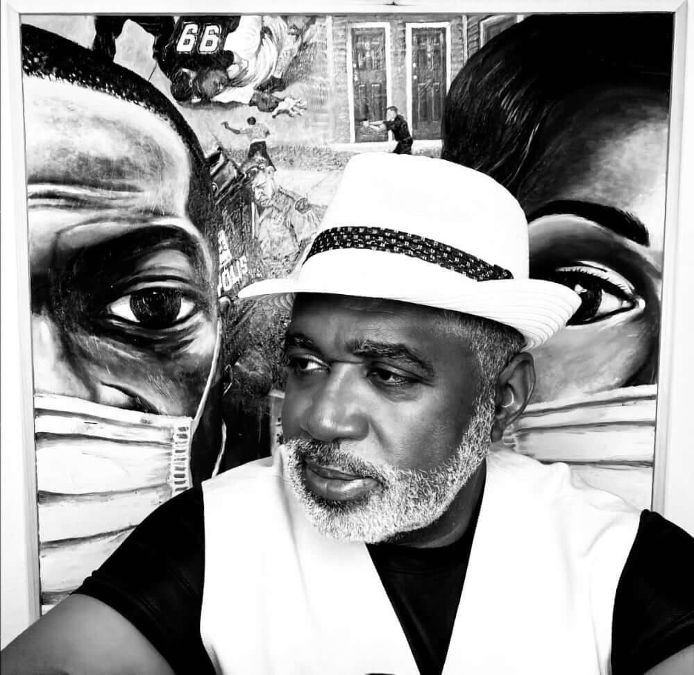 A black and white image of a dark-skinned African American man with a mingled gray beard wearing a white hat with a black hatband, a white suit vest, and a black t-shirt. He is in a three-quarter pose in front of a painting entitled, "Why I Can't Breathe."