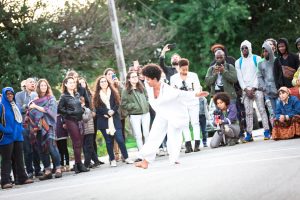 Onye Ozuzu, wearing white flowing clothes, dances outdoors in front of a crowd