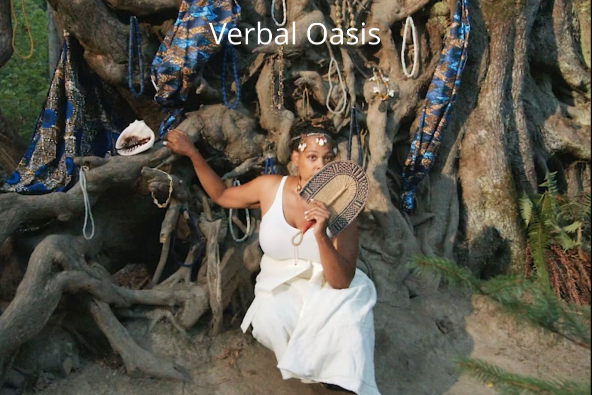 A brown-skinned woman wearing a white dress and a headband decorated with white pendants poses outdoors in a sitting position against the large, gnarled tree root system of an ancestral tree. She holds a decorative handheld fan up to her face, covering her mouth and part of a cheek, and rests her other hand slightly behind her on one of the tree's large roots. The ancestral tree, its base at least ten feet in diameter, is so wide that it fills most of the frame behind her, and it is decorated with draped blue and gold patterned fabric, necklaces, beads, and a large conch shell. The prominent white text "Verbal Oasis" is overlaid at the top of the image.