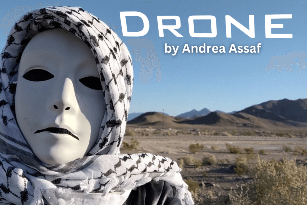 A masked figure with a death-white face, solid black eyes, and a down-turned mouth, wearing a black leather jacket and a keffiyeh (black and white patterned headscarf). The figure stands in front of a desert landscape with blue sky, patchy desert greenery, and distant mountains. Text above the image reads: “DRONE by Andrea Assaf.”