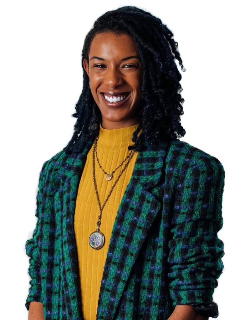 An image of a medium light-skinned, Black woman with dark brown locs wearing a yellow shirt, blue and green plaid blazer, and locket jewelry around her neck.