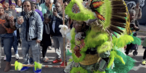A Black man, Ivan Watkins, poses in an elaborate green feather head-to-toe Black Masking Indian costume.