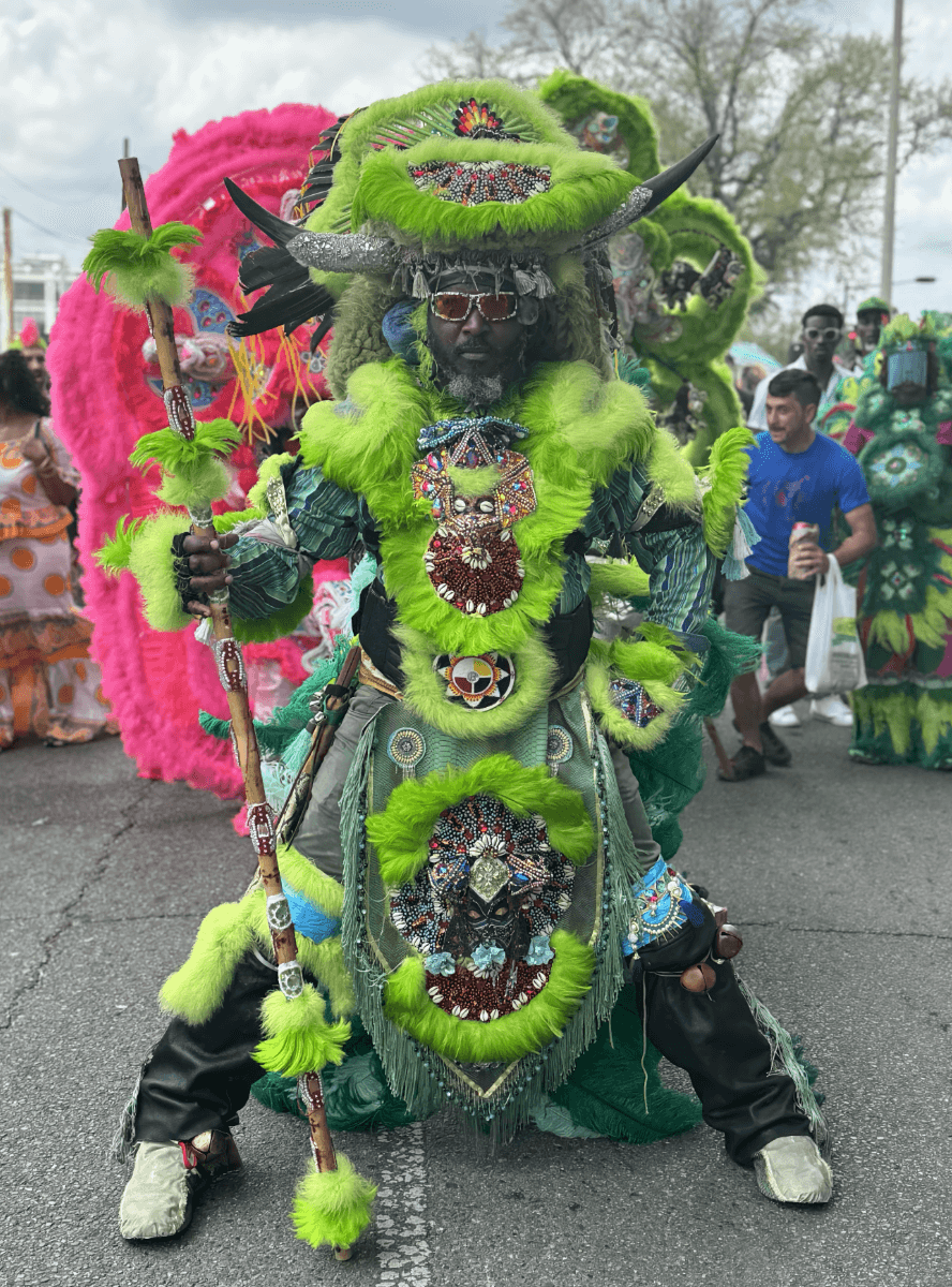 A Black man, Ivan Watkins, poses in an elaborate green feather head-to-toe Black Masking Indian costume.