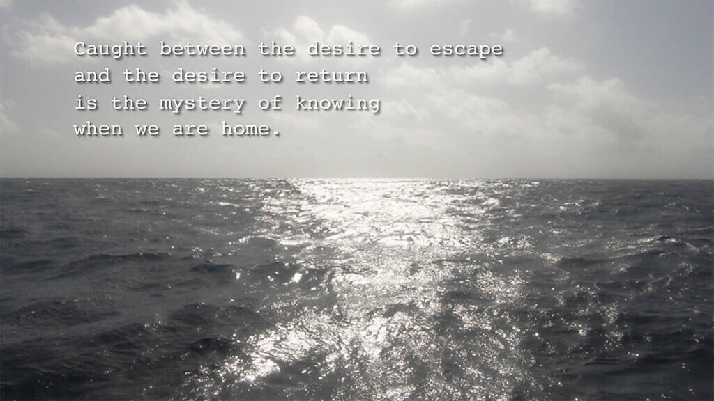 A grayscale photo of the ocean surrounding the Island of Barbados. White clouds hang above the sea, and the sea reflects the sun on the water. The water is calm but has movement within the photo. Typed across the top of the photo are the words: 'Caught between the desire to escape and the desire to return is the mystery of knowing when we are home.'