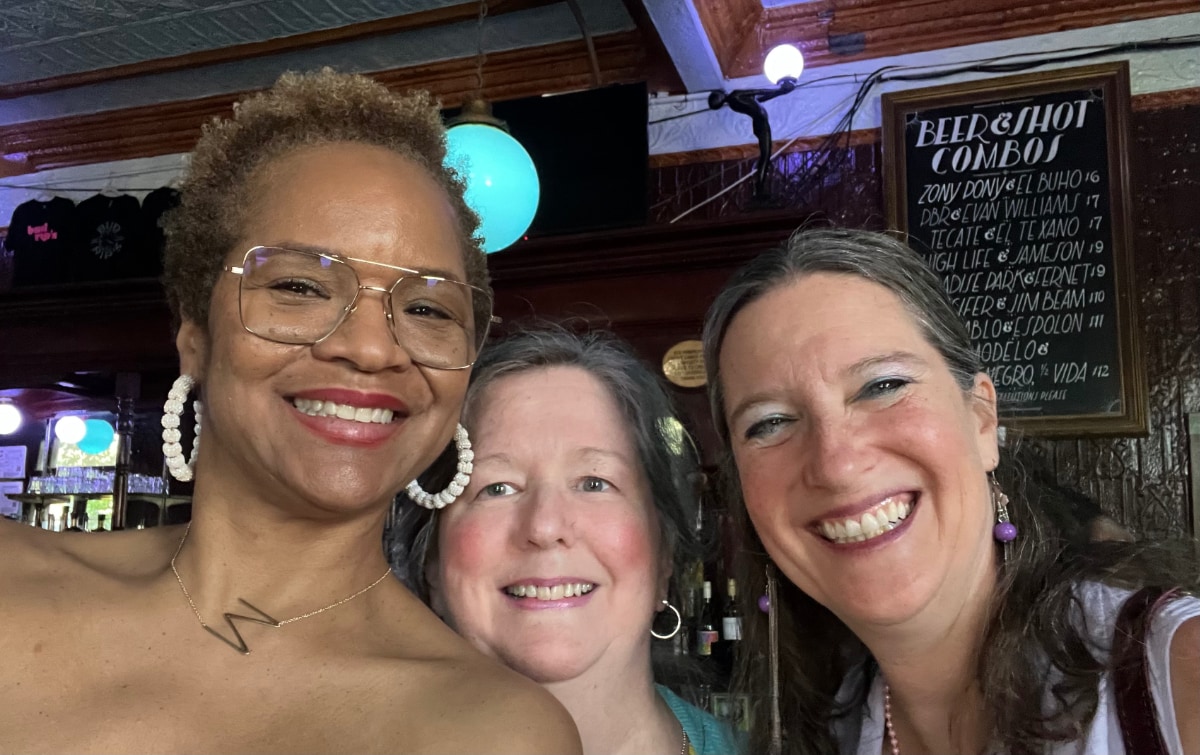 Stephanie Atkins, a Black woman, poses for a selfie next to two white women in a restaurant during the daytime.