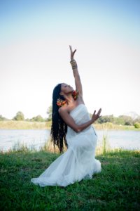 Jarrell Hamilton, a medium-dark skinned woman with long braids, dances in the grass of a riverbank.