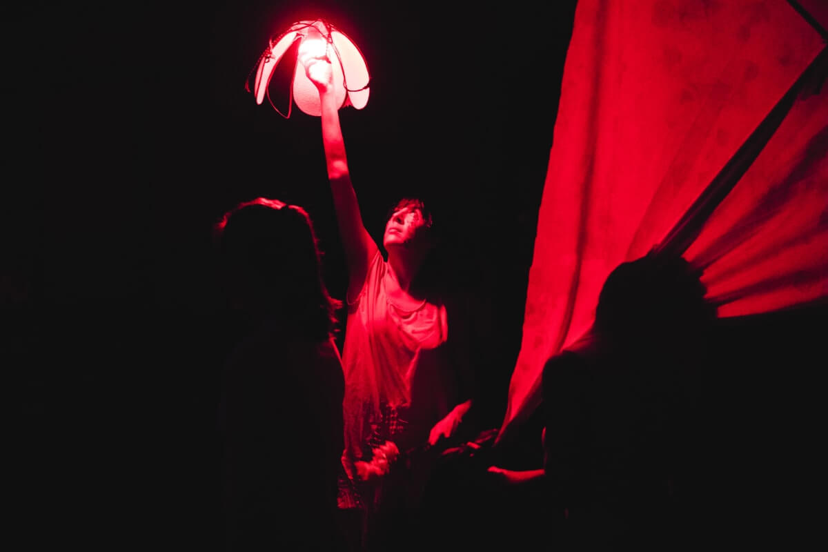 a dancer bathed in red light reaches up and changes a light bulb.