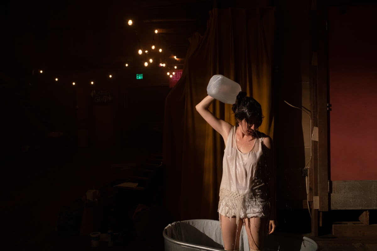 A dancer pours a jug of water on her head.