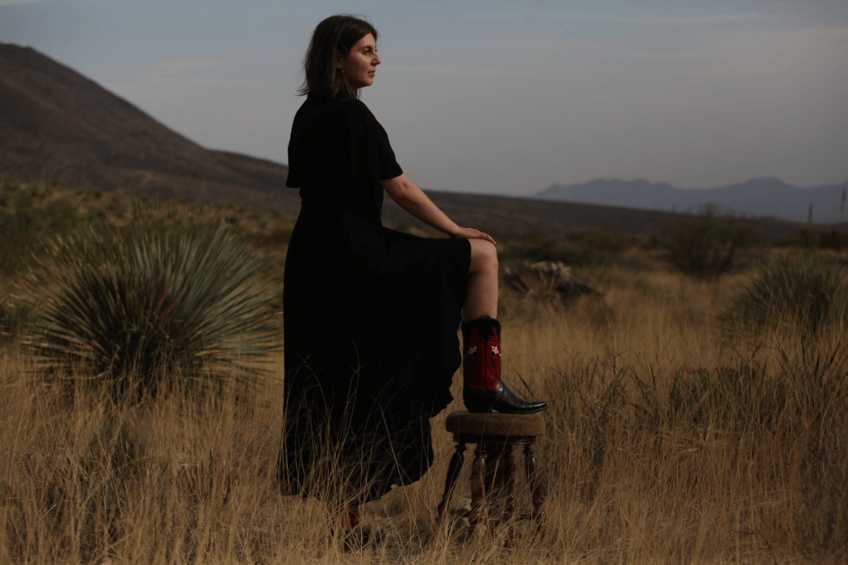 Amanda Ekery in a black dress and cowboy books looking out at the Franklin Mountains in El Paso, TX