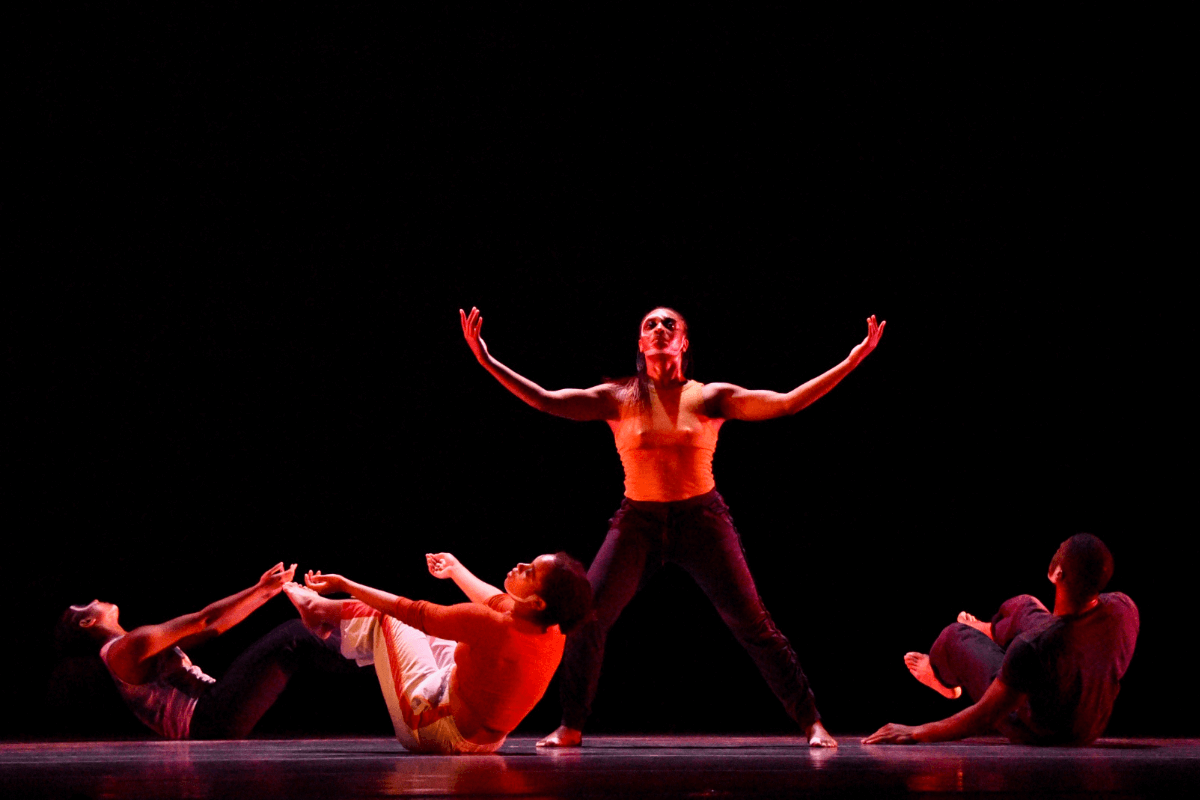 Three figures plead around a standing performer, arms extended in a sea of red.