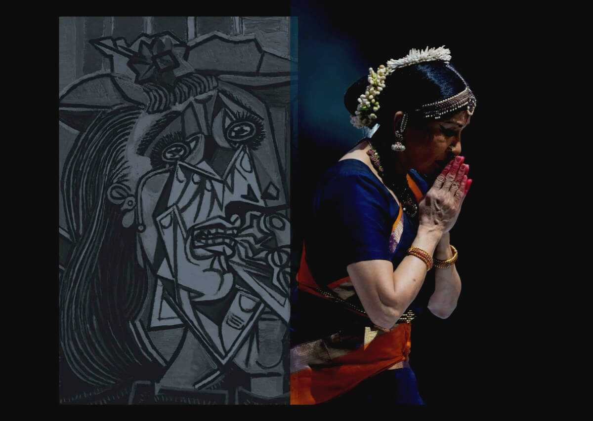 One woman is in a prayer position in front of a gray Picasso-esque painting. She is wearing flowers in her hair, a short sleeved blue shirt and a red sash.