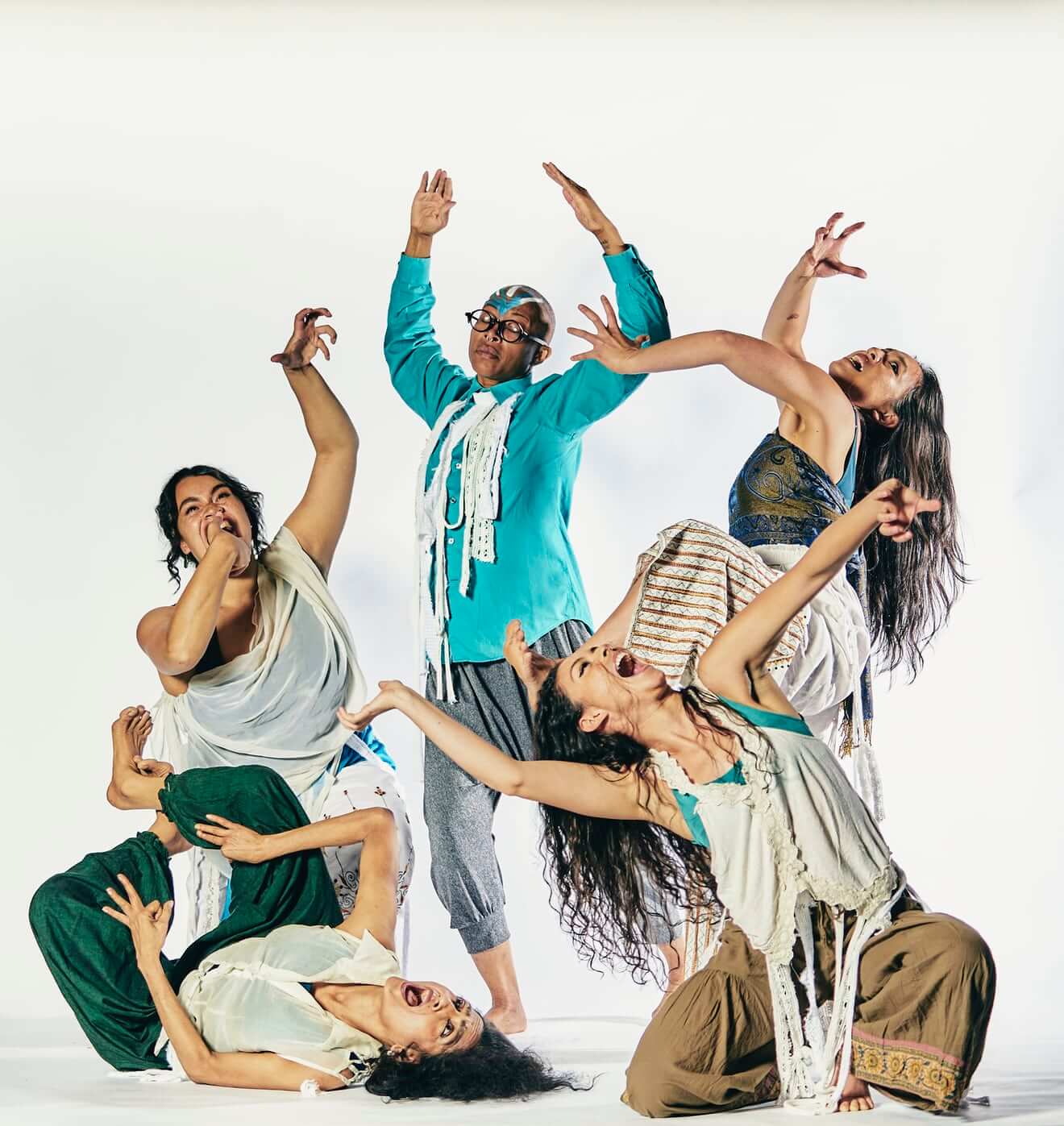 Five BIPOC women and femmes, attired in loose-fitting costumes, dance at different levels of height, their arms reaching to embrace the air, and their faces reflecting strong vocal expressions.