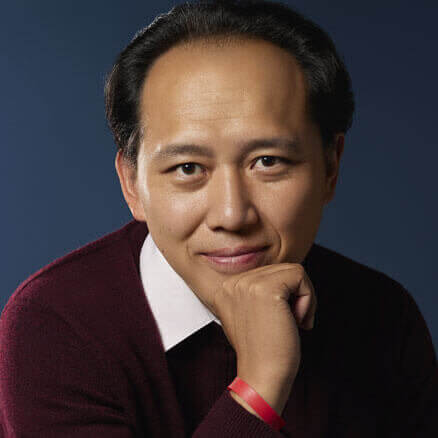 Haowen is a Taiwanese man with wavy black hair, brown eyes, and a light-medium complexion. Sitting with one arm resting on his knees and the other on his chin, he is smiling intently at the camera. He is in a dark blue backdrop and wearing a wine-red sweater, blue jeans, with a wristband and a silver wristwatch.