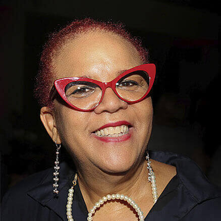 Headshot of Rosie Gordon-Wallace. Black woman in red glasses, red hair pulled back, head tilted in a moment of bliss. Beautiful pearl necklace, gifted by my son, Gordon, and vintage pearl drop earrings. Body covered in COS Black satin cotton dress.