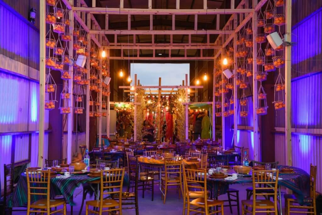 A 100ft train shed. Inside: several tables set, ready for dinner, in the background oranges hanging in baskets from a tall wooden structure.