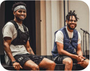 In this Image is two African American Men sitting on a stage after a live performance. On the Left hand side is Marcell Johnson With afro and white bandana, White t shirt with black vest and black shorts and white sneakers Host and Mc of the Yes Foundation Violence Prevention Symposium , on the right hand Side is Yusef Shelton with white t shirt, blue vest, black shorts, blue, black and white nike sneakers, who just Mc'd and performed music at Yes foundation Symposium where the pair end up being on local news station for their participation and involvement in bringing culturally relevant educational, fun and engaging energy to event held at Pitt University in collaboration with Pennsylvania number one violence prevention organization. Shot by Reece Miller.