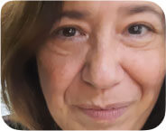 Selfie of woman with light brown face close up, medium brown hair, looking straight into the camera, slightly smiling with mouth closed, green large tropical leaves in the background.