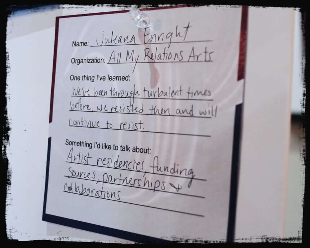 Close-up photo of a handwritten “dance card” pinned to a board, filled out by Juliana Enright from All My Relations Arts. It reads: “One thing I’ve learned: We’ve been through turbulent times before, we resisted then and will continue to resist.” Under “Something I’d like to talk about,” she lists: “Artist residencies, funding sources, partnerships & collaborations.”