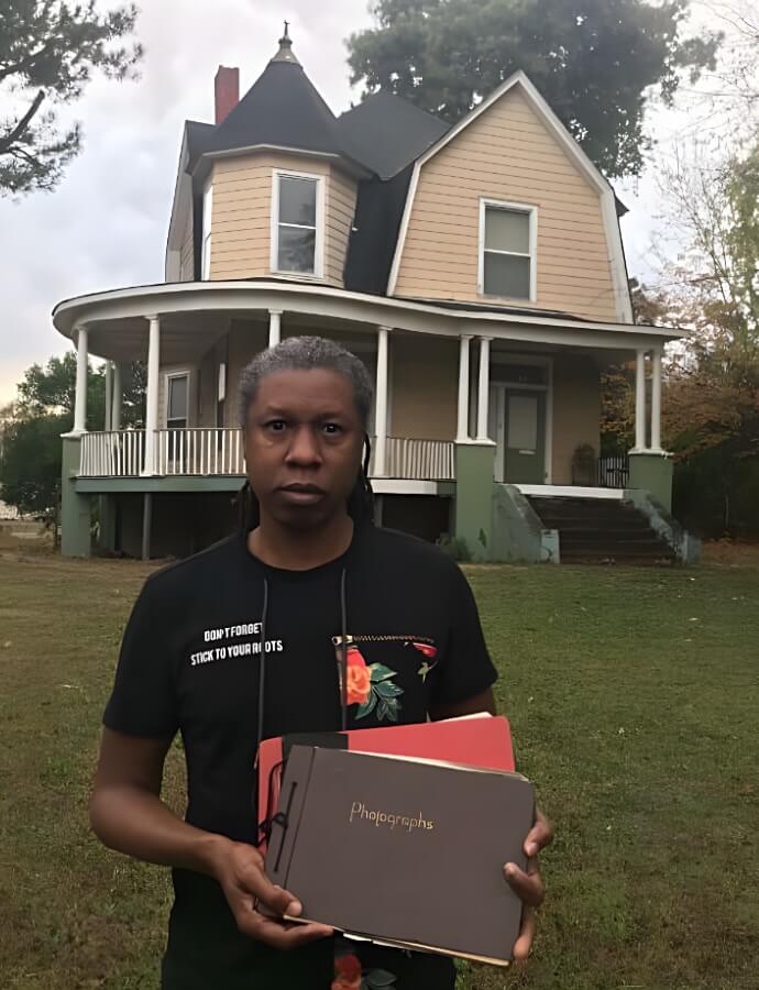 Jahni Moore standing in front of the Drake House holding vintage photo books.