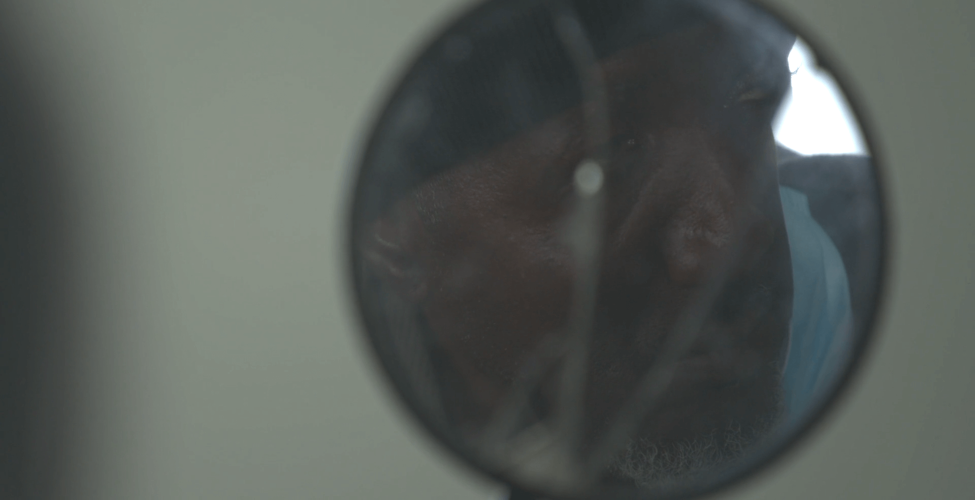 In this still from the film "after angola," a indeterminate shape is partially visible through a circular lens. The image is dimly lit and out of focus so that the details aren't clear.