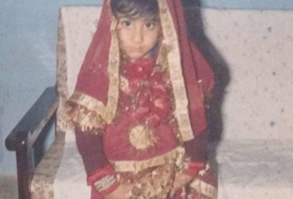Adil Mansoor as a child in a red and gold tunic with a matching scarf draped over his head
