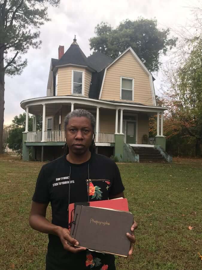 Jahni Moore standing in front of the Drake House holding vintage photo books.