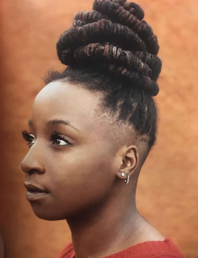 A dark-skinned Black woman with long locs shaped into a bun.